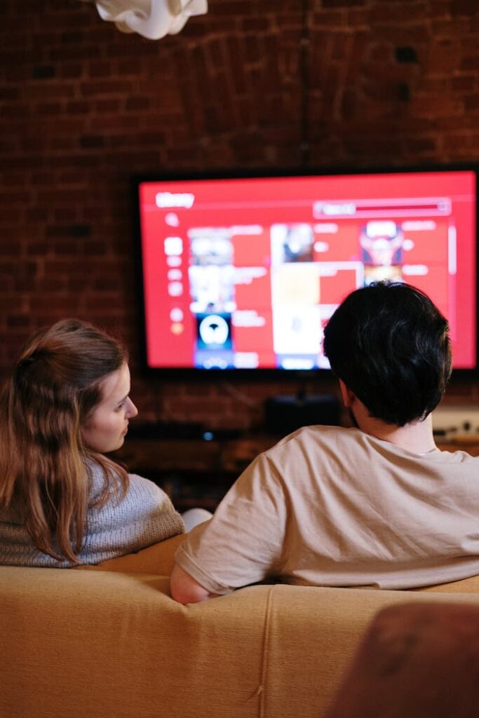 A couple sitting together in a cozy living room, watching a movie on a smart TV.